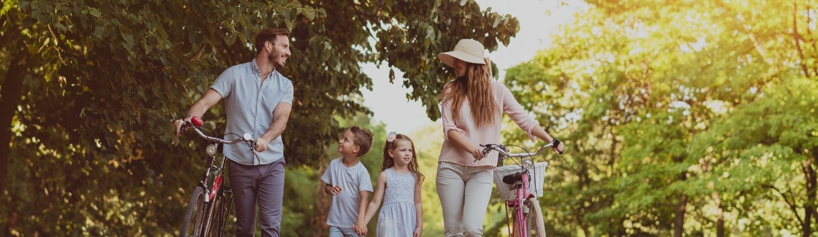 Family of four walking through park with bicycles