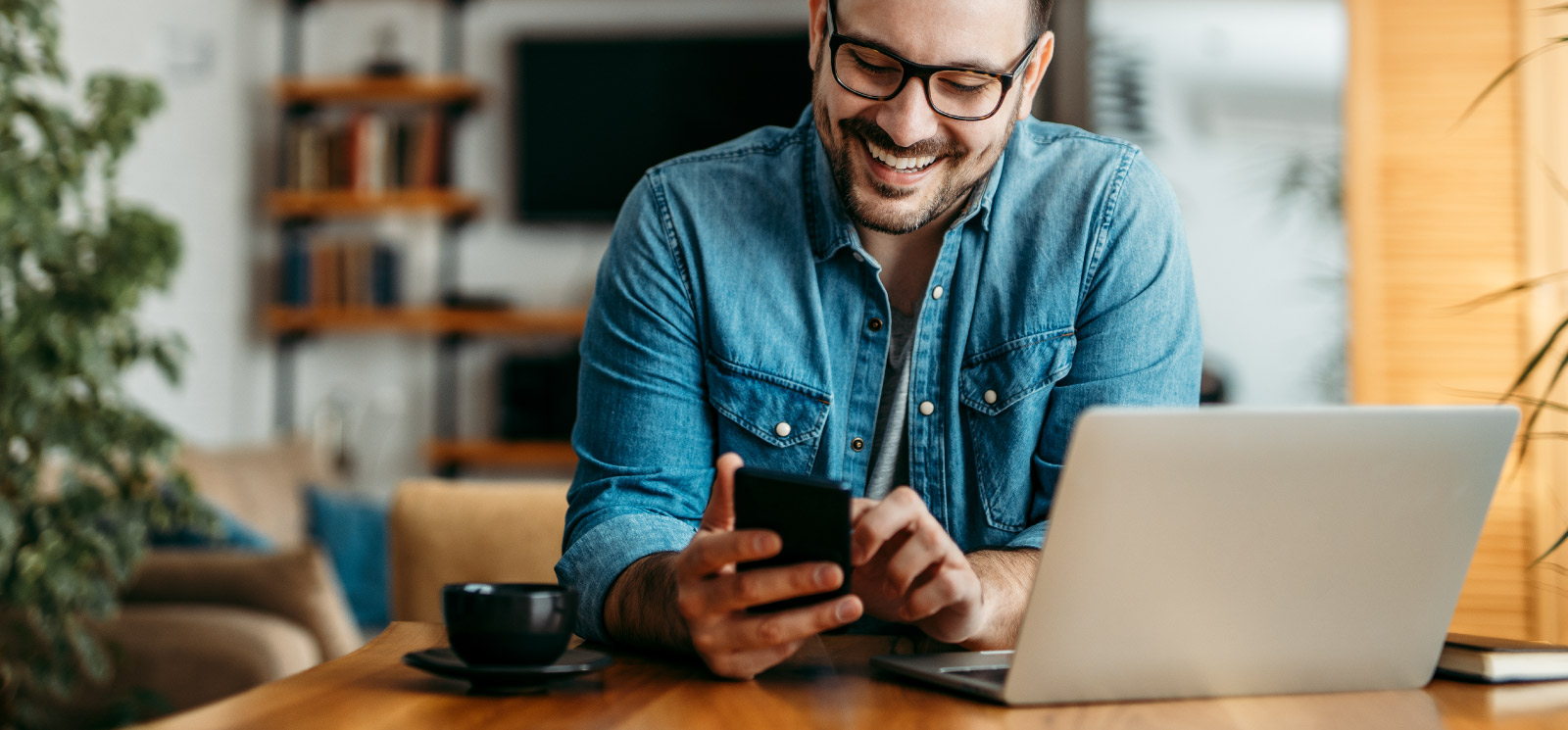 Man happily looks at his phone while sitting in front of his computer